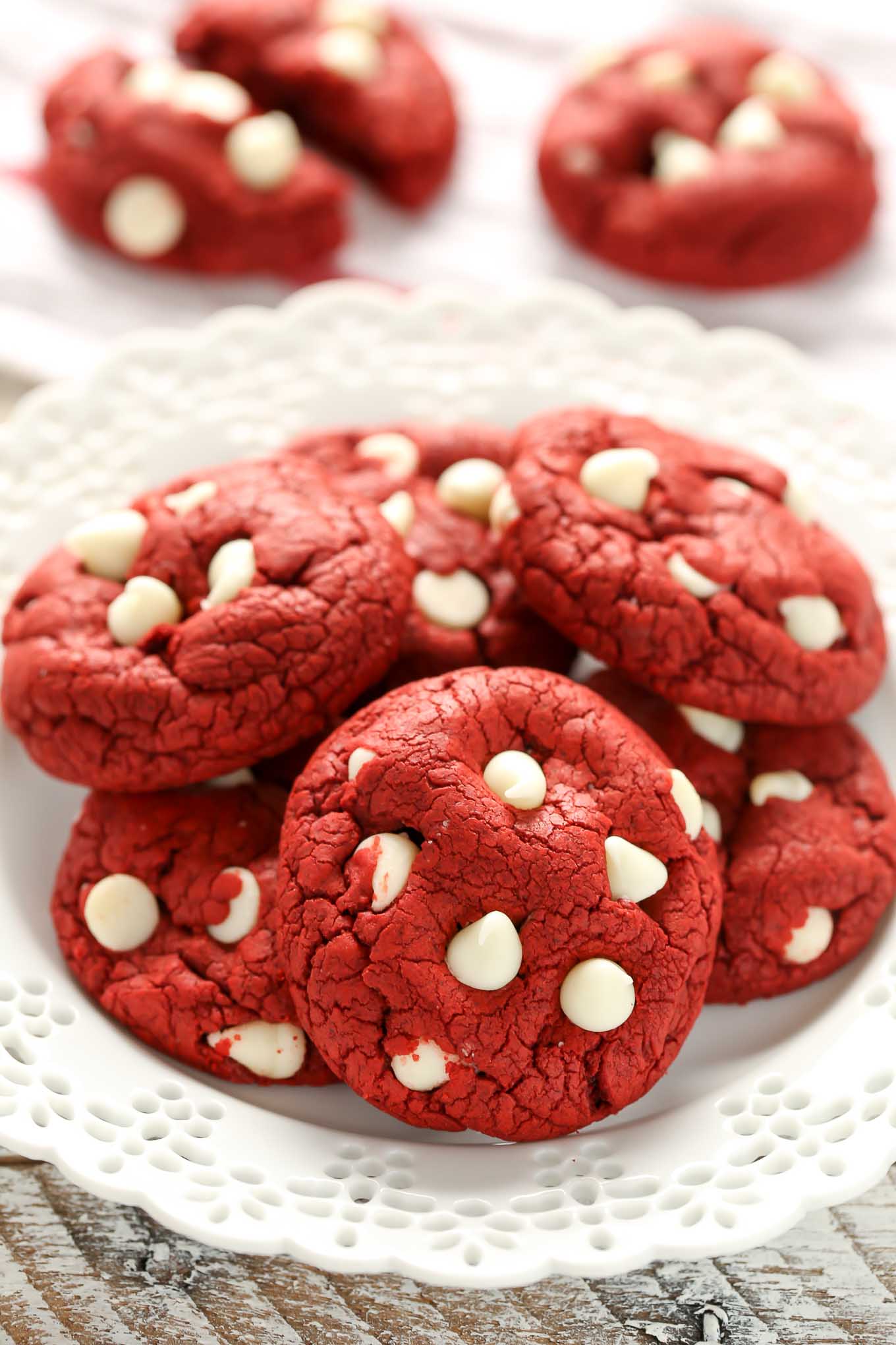 A white plate piled high with red velvet cookies. Two extra cookies rest in the background. 